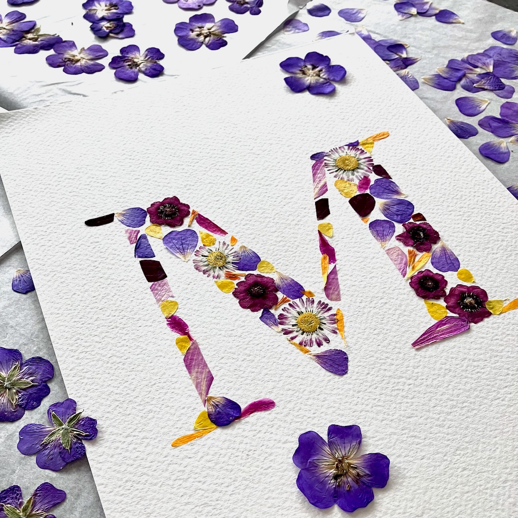 Herbier personnalisé en forme de lettre M avec des fleurs de géranium 'Rozanne' séchées.